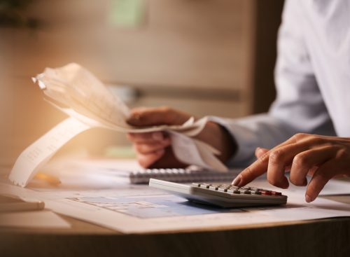 Close-up of economist using calculator while going through bills and taxes in the office.